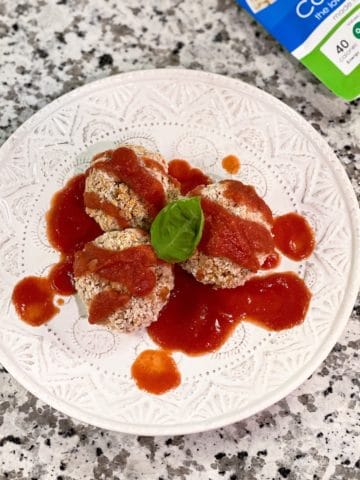 3 baked cauliflower rice balls drizzled with tomato sauce, topped with basil on a white plate