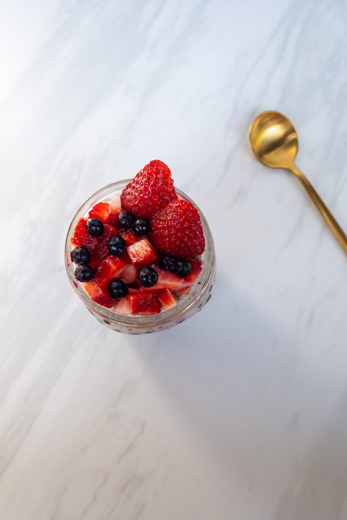 Chia seed pudding with strawberries and blueberries overhead view with a white marble background and gold spoon