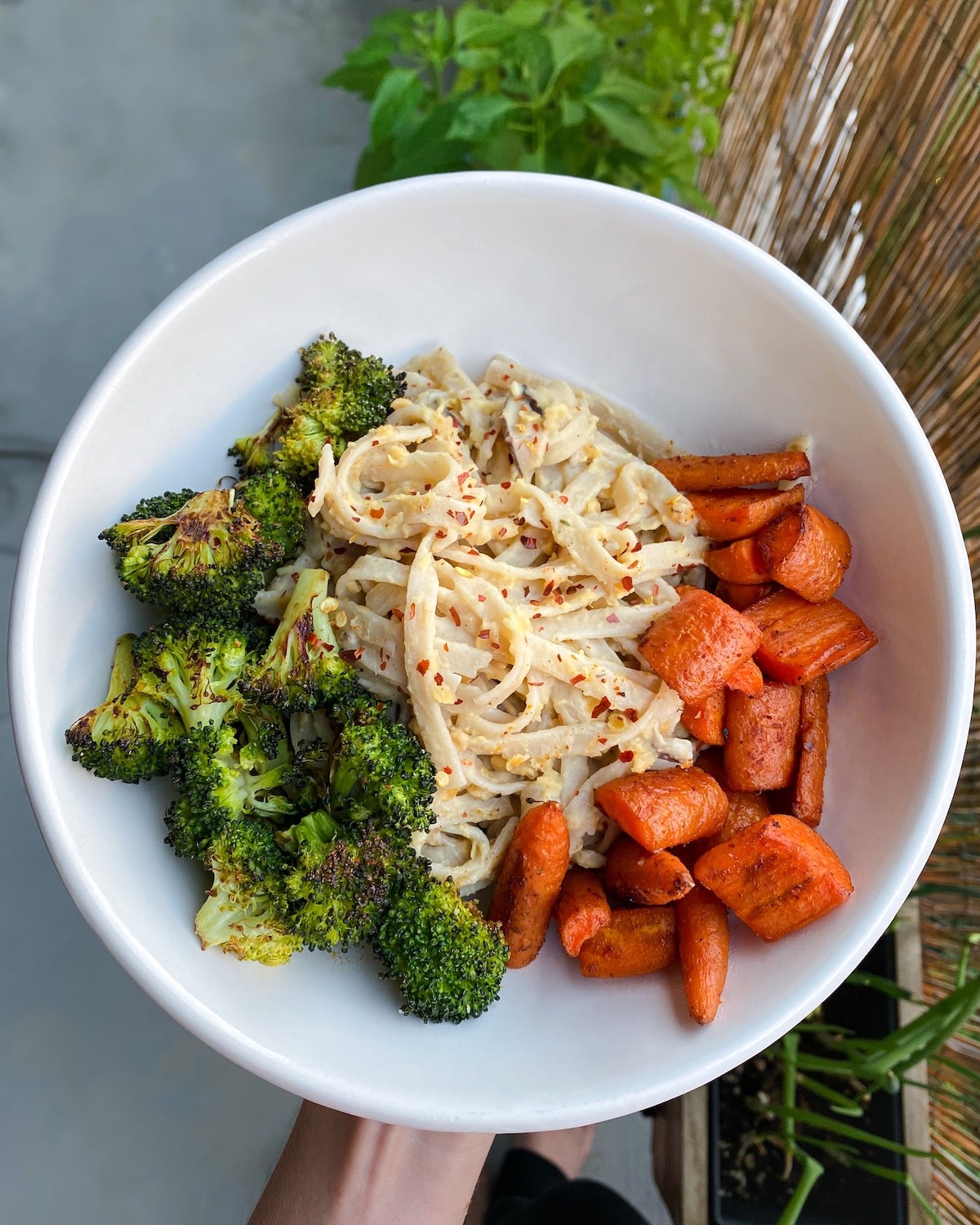 white bowl with charred broccoli, carrots, and vegan truffle fettuccine alfredo pasta topped with red chili flakes