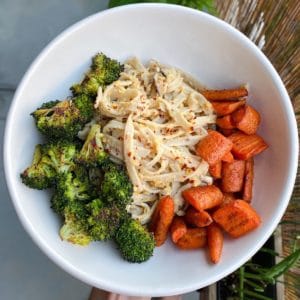 white bowl with charred broccoli, carrots, and pasta topped with red chili flakes