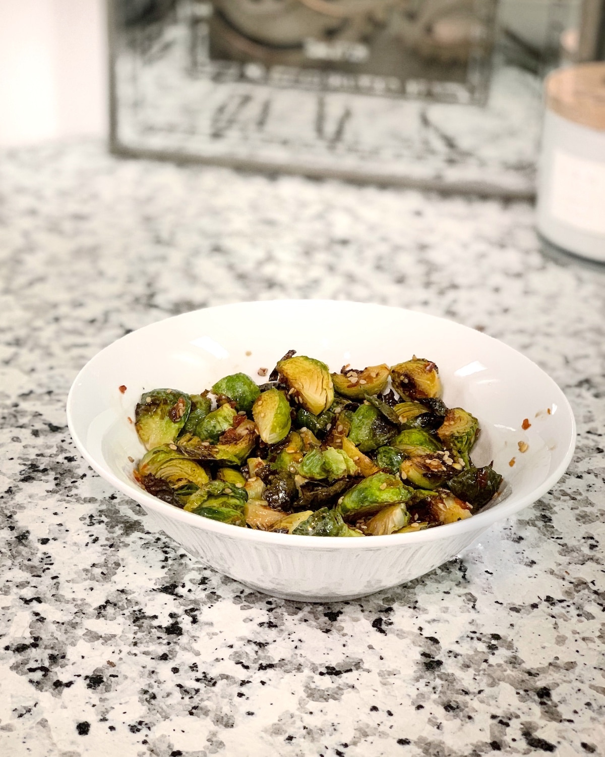 Asian maple glazed brussel sprouts in a white bowl on a marble counter.