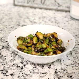 Asian maple glazed brussel sprouts in a white bowl on a marble counter.