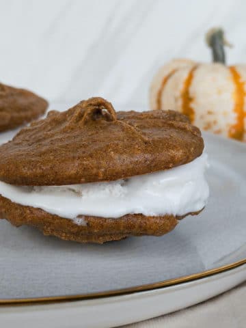 Side angle of whoopie pie on plate with pumpkin in background