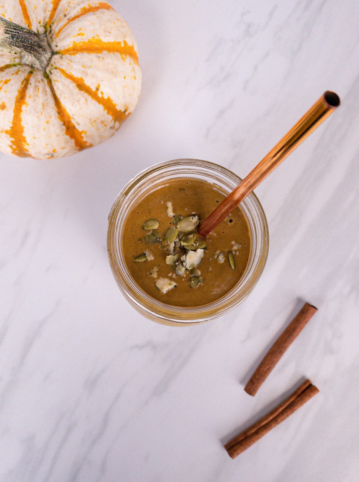 Pumpkin pie smoothie top with crushed pumpkin seeds with cinnamon sticks and pumpkin in the background
