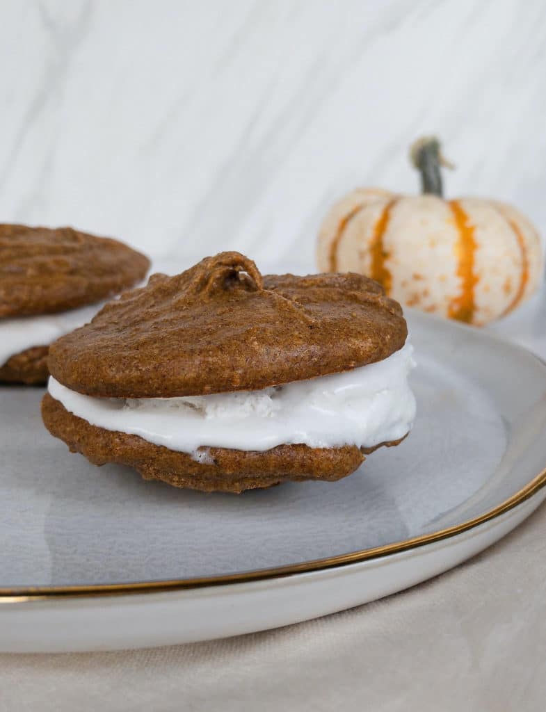 Side angle of whoopie pie on plate with pumpkin in background