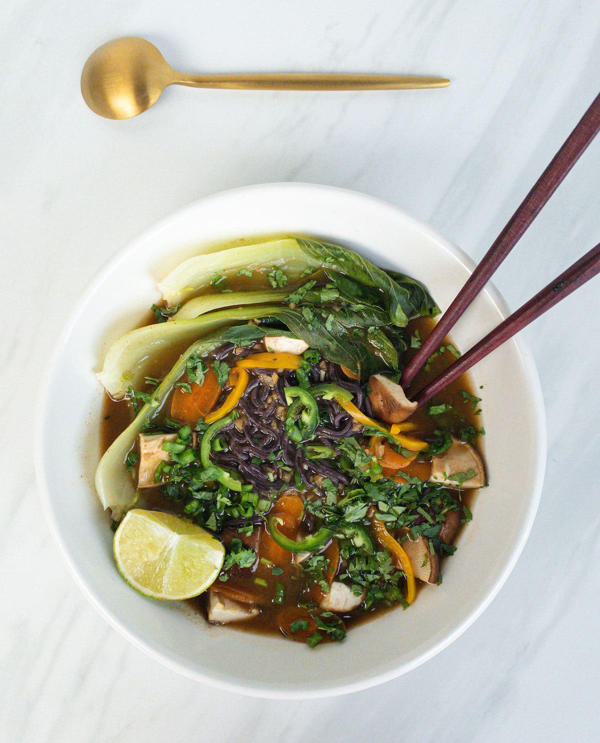 overhead view of vegan pho with vegetables in white bowl with chopsticks