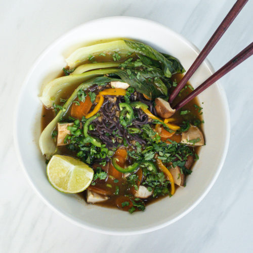 overhead view of vegan pho with vegetables in white bowl with chopsticks