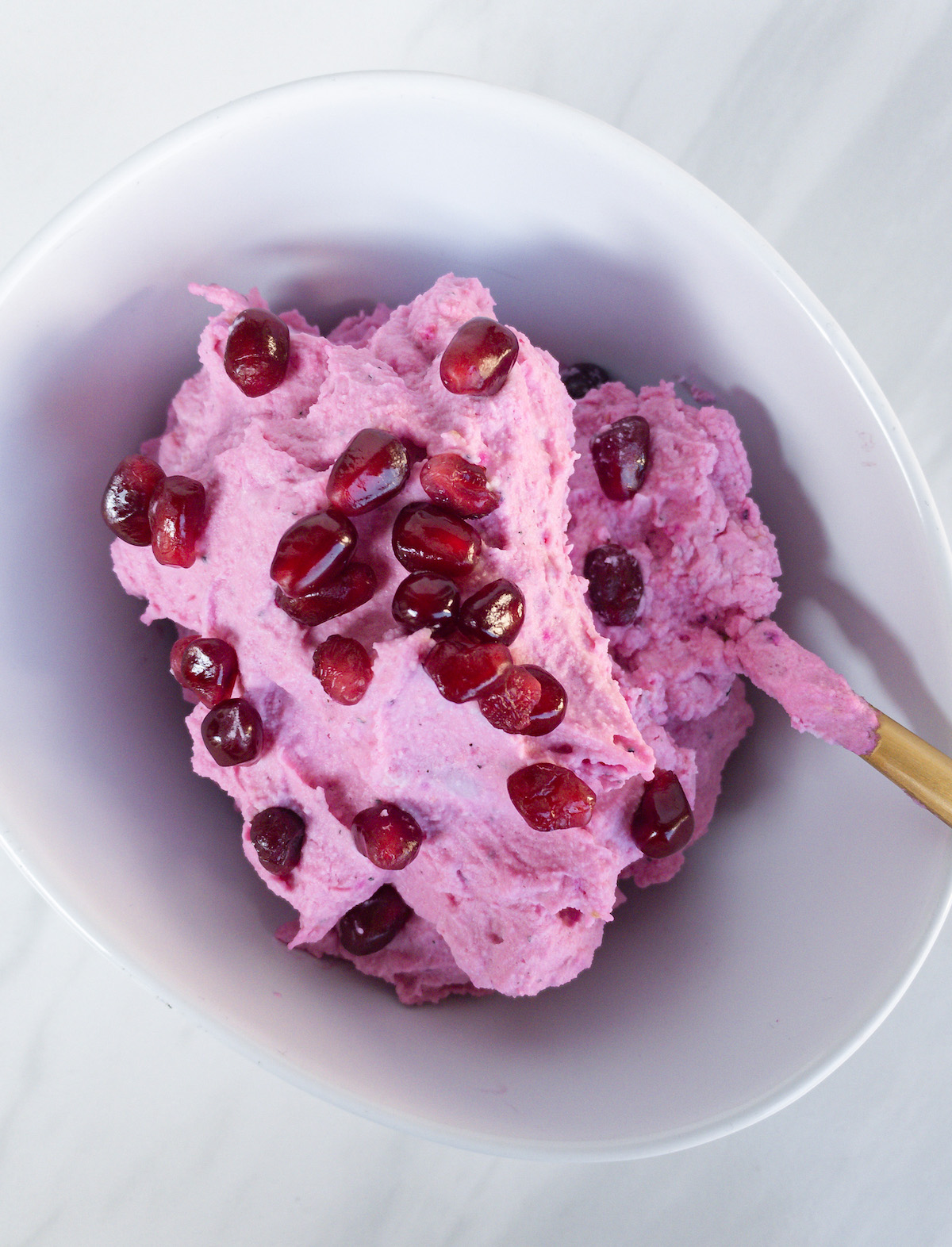 pink whipped cream with pomegranate seeds in a white bowl