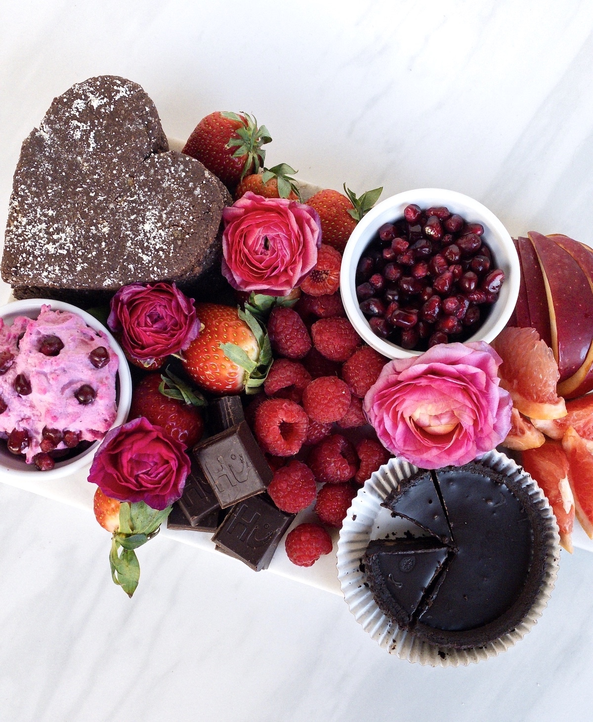 Pink, red, and brown charcuterie board filled with fruit and chocolate.