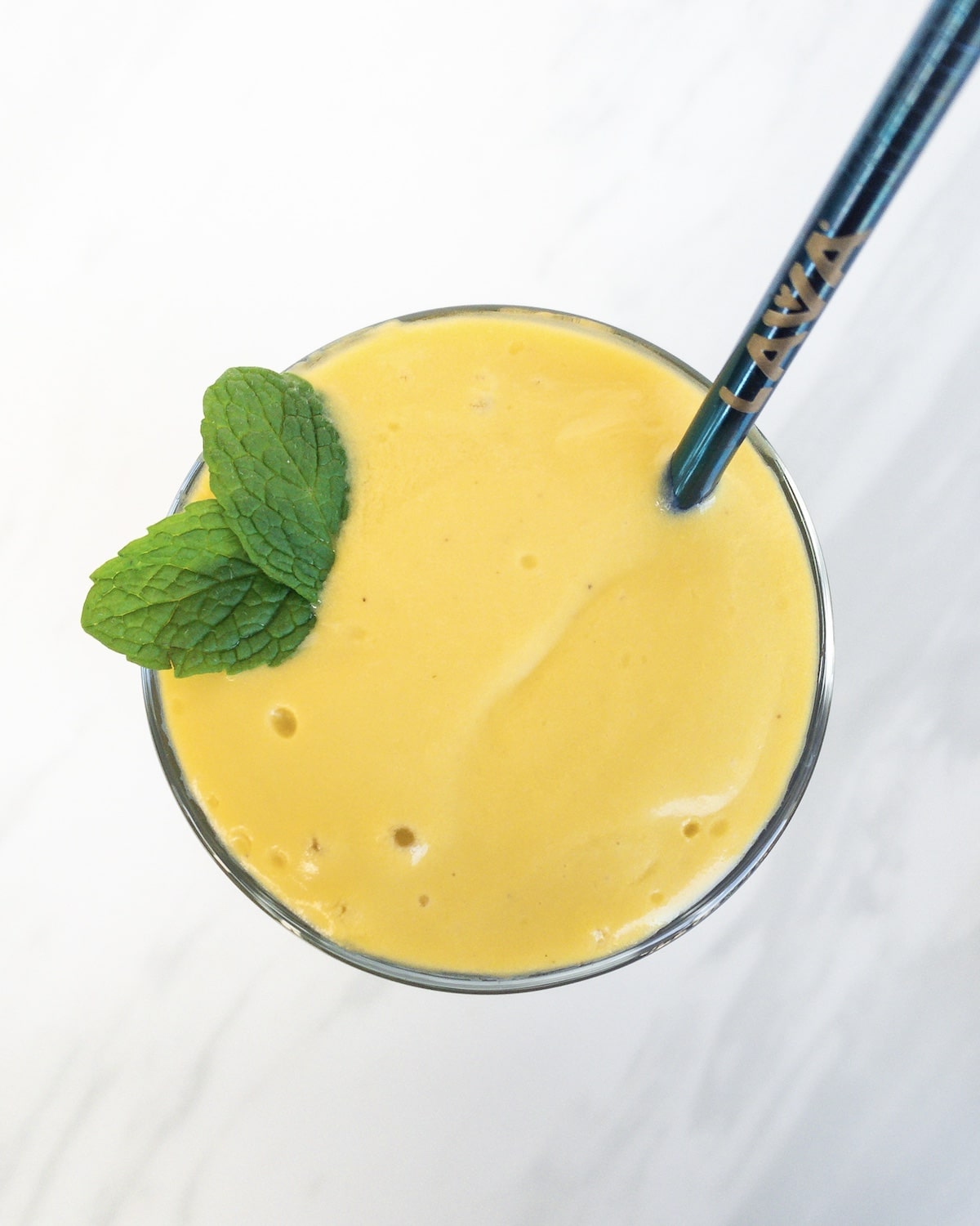 Bright yellow mango lassi with green mint leaves and blue straw