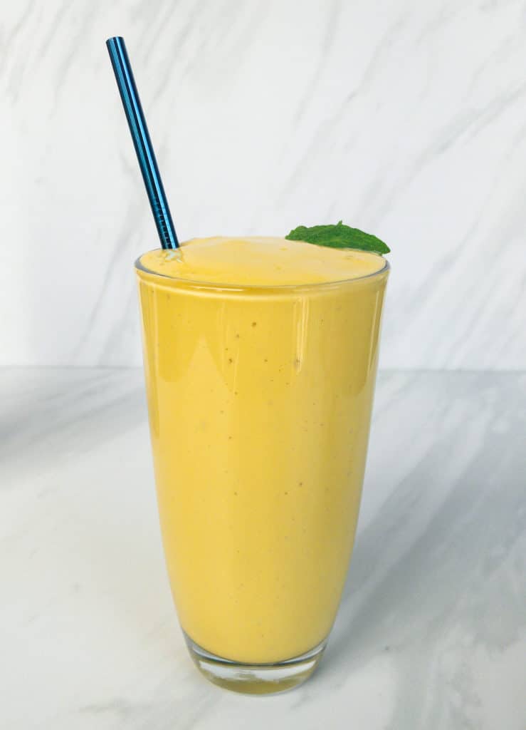 Bright yellow mango lassi with green mint leaves and blue straw