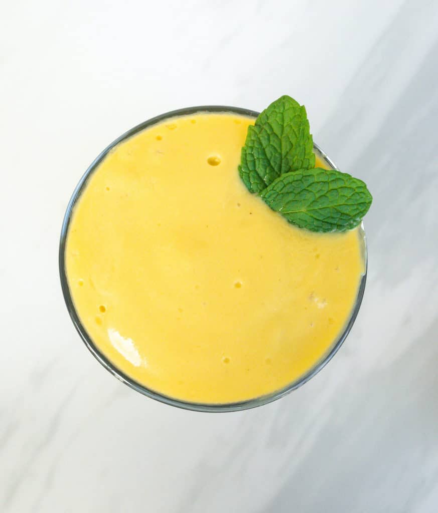 Bright yellow mango lassi with green mint leaves