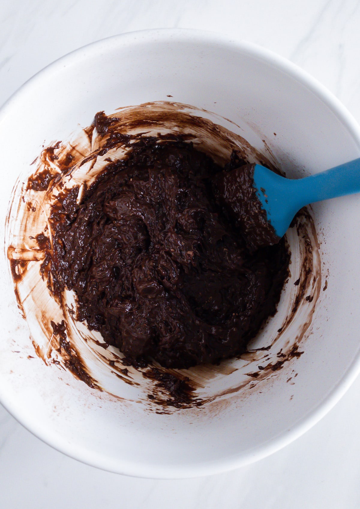 brownie batter in white bowl with blue spoon