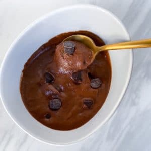 Chocolate ice cream in white bowl with gold spoon scooping