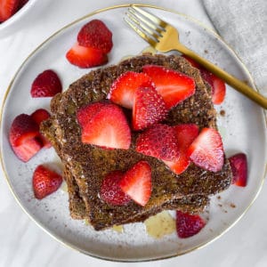 Healthy vegan gluten free golden brown french toast with bright red strawberries on top